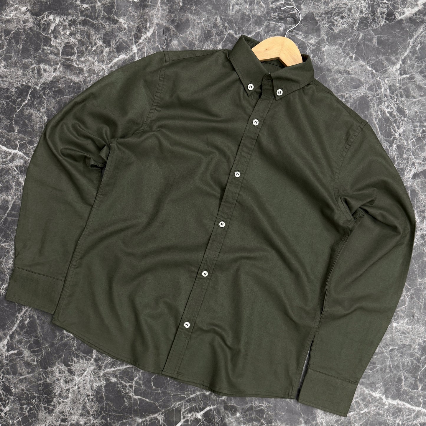 Green shirt on a wooden hanger against a gray marble background